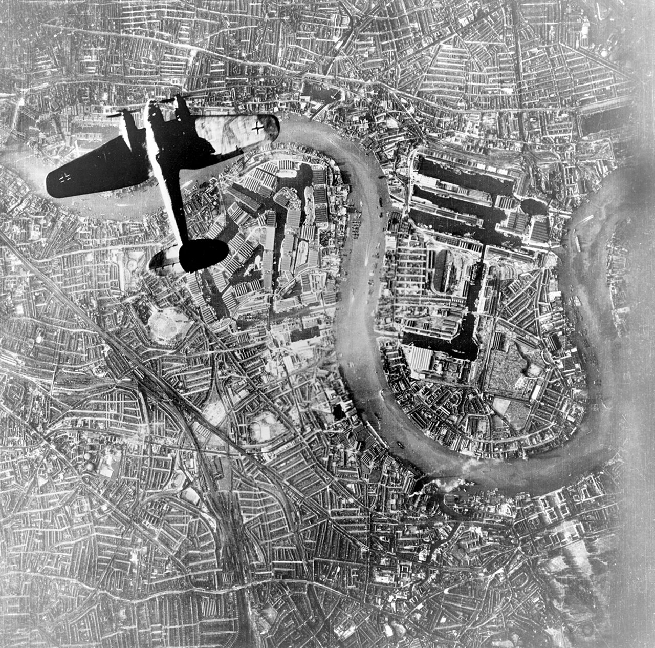 A German bomber photographed from above, silhouetted against the loop of a river and dock basins