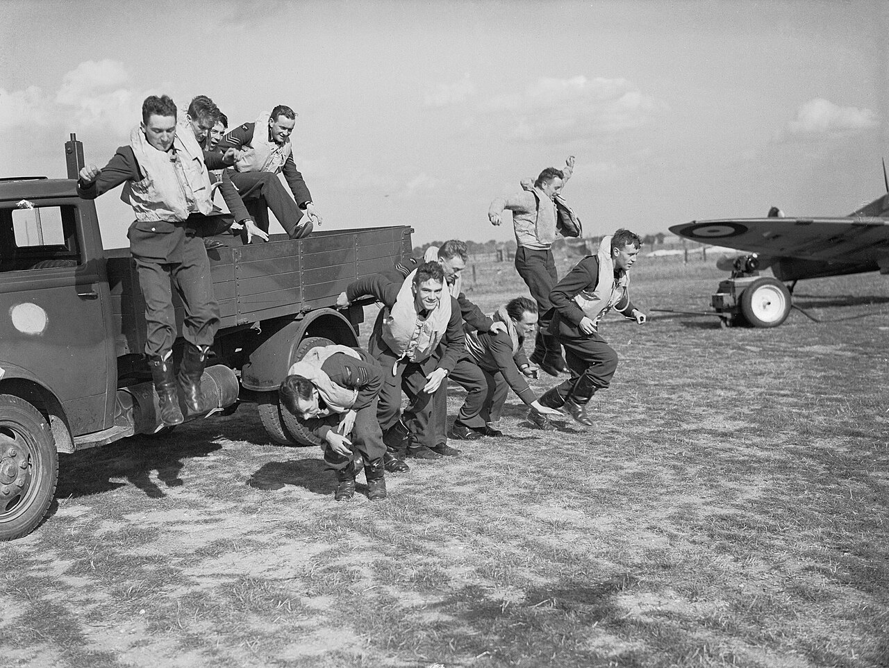 Pilots in flying kit jumping down from the back of a truck beside parked fighters