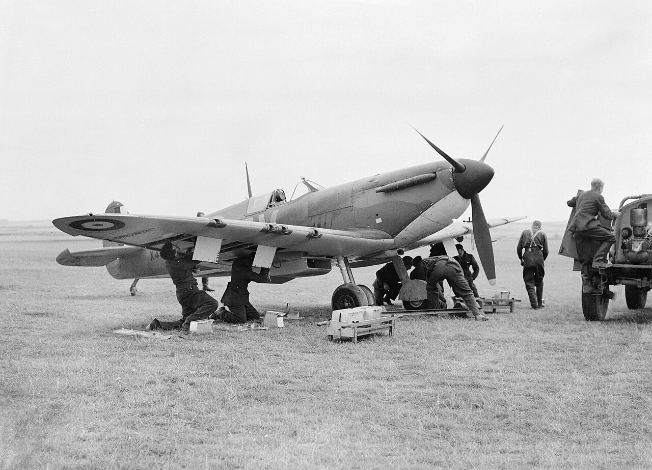 Ground crew working on the wing of a Spitfire with ammunition belts laid out on the grass