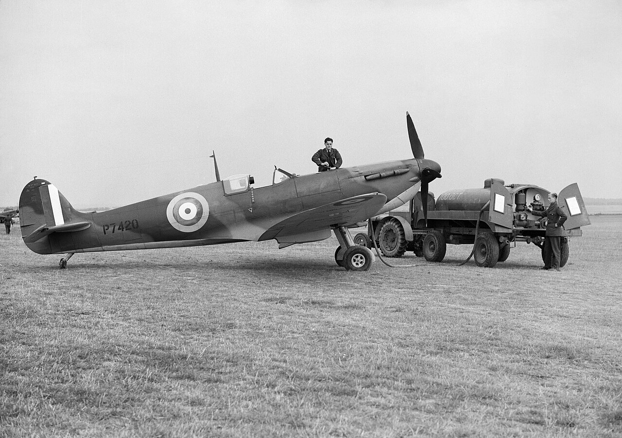 A fuel bowser drawn up beside a Spitfire while ground staff work at the fuselage