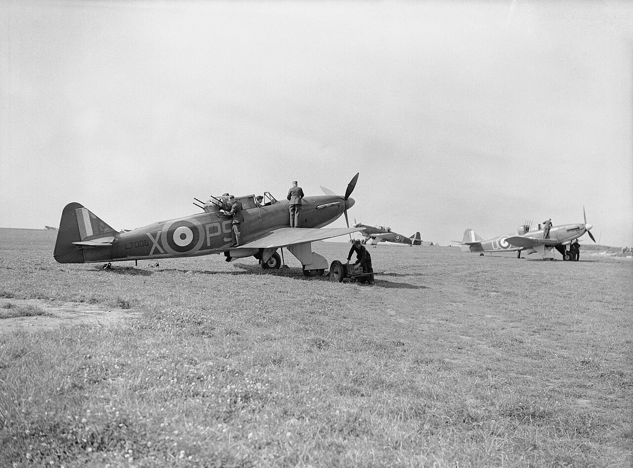 A single-engined military aircraft with a gun turret behind the cockpit, on a grass airfield