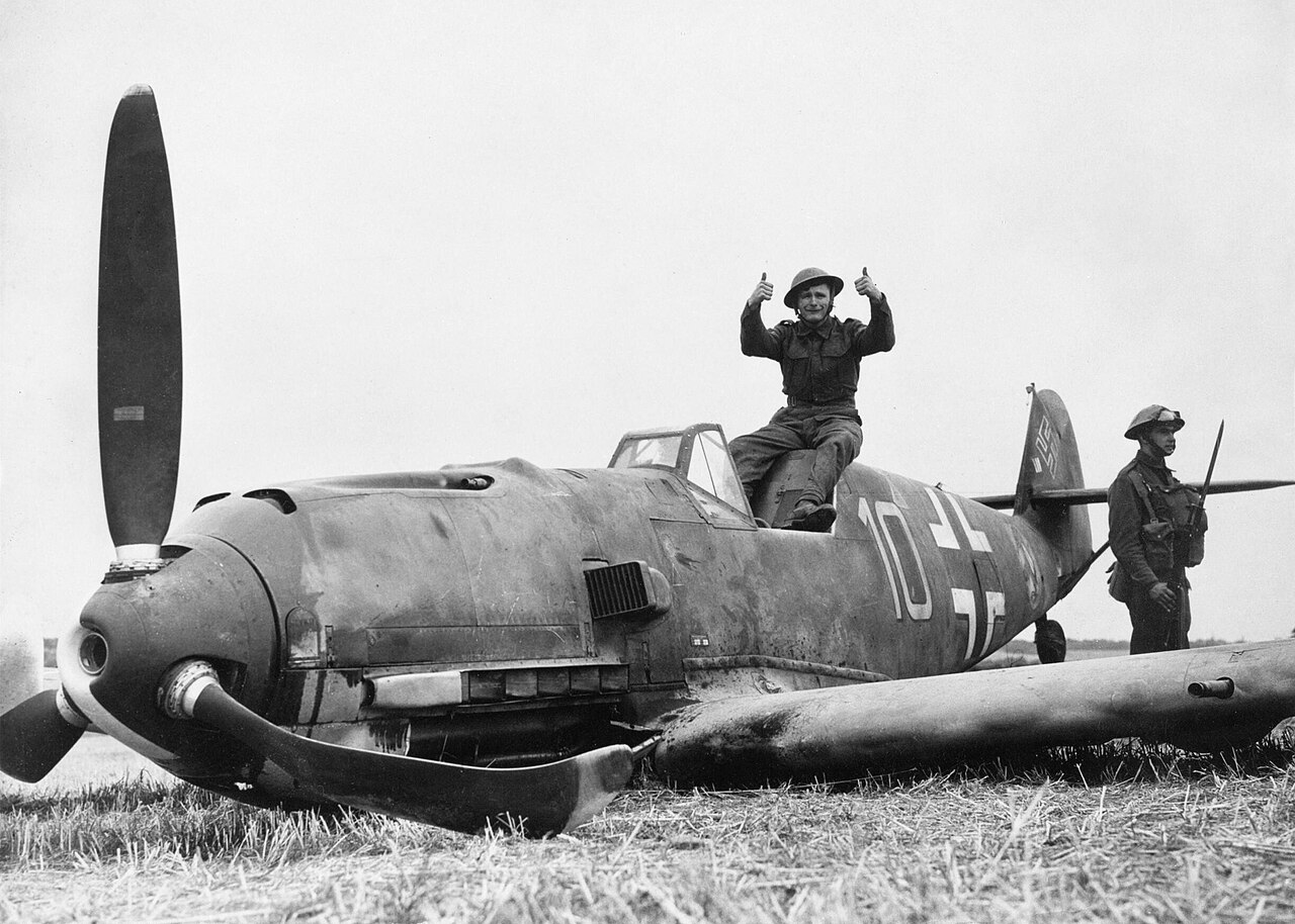 Soldiers standing on and beside a crash-landed German fighter in a field
