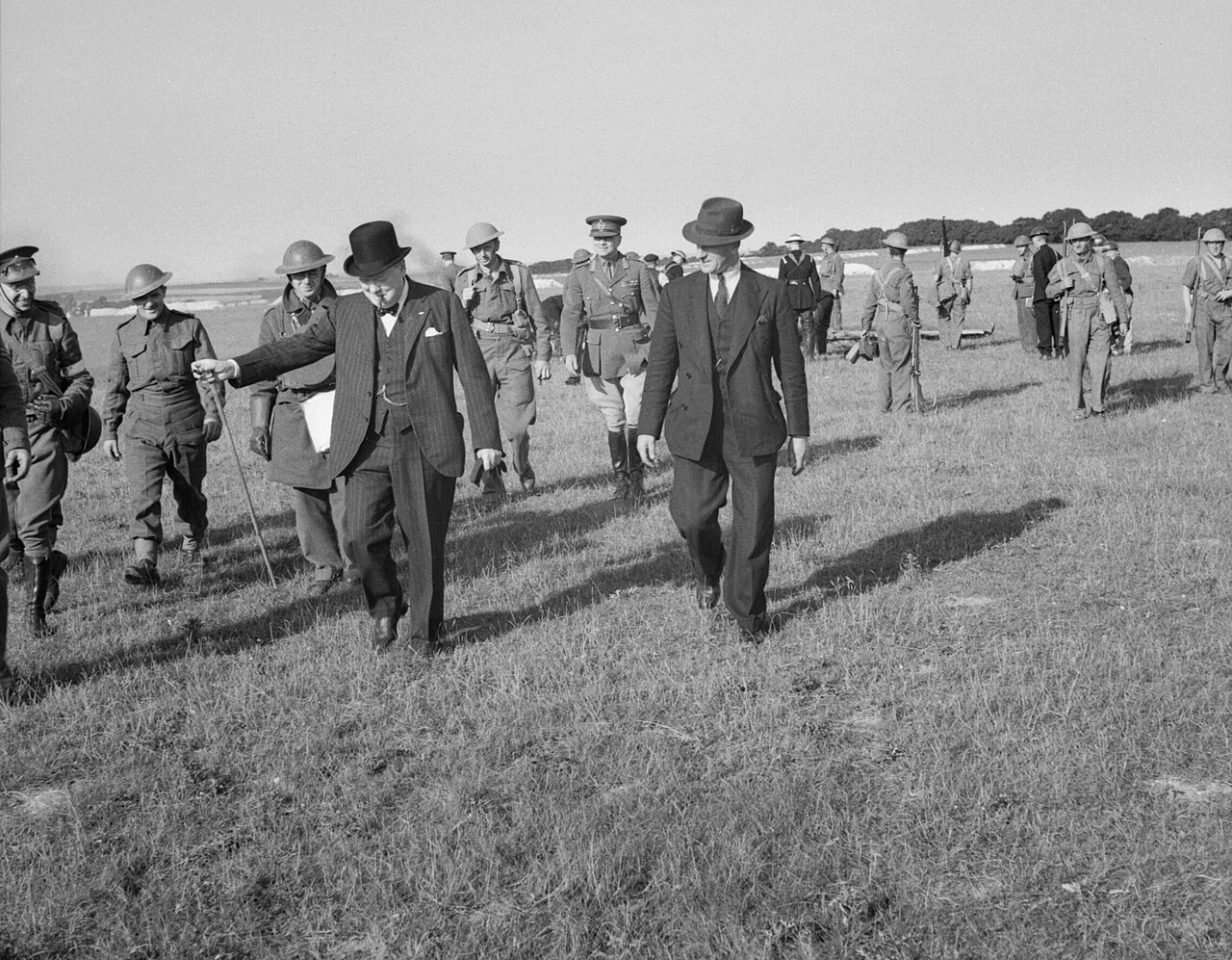 Churchill and a group of officials walking across a field away from an aircraft wreck