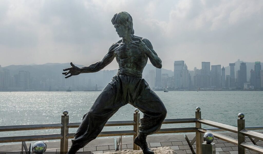 The bronze statue of Bruce Lee in a fighting stance on the Avenue of Stars in Hong Kong, with Victoria Harbour and the city skyline behind it