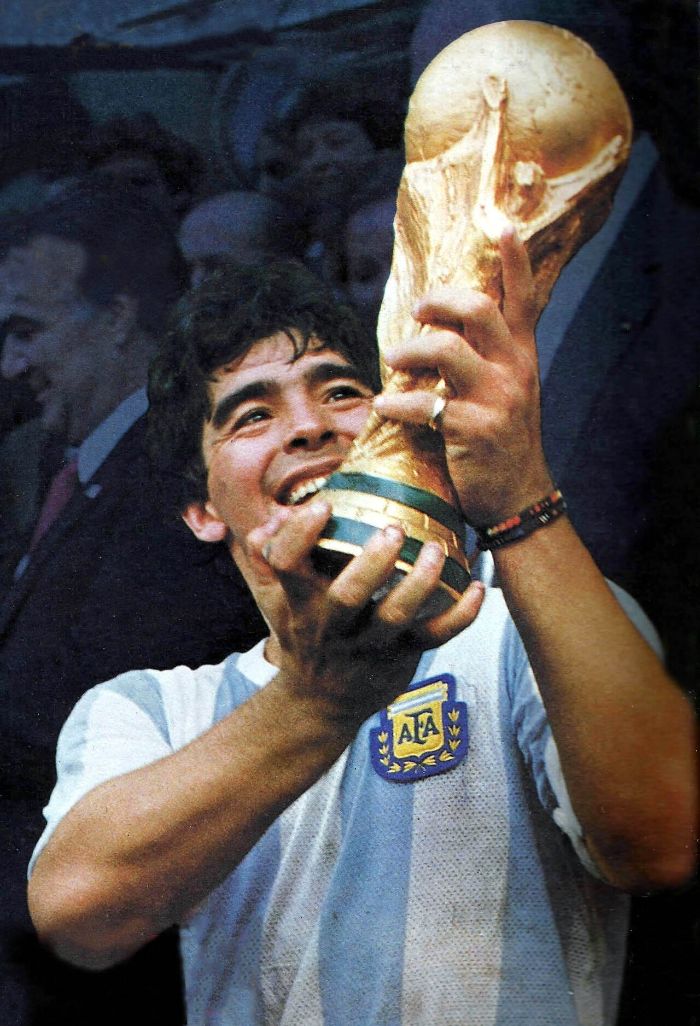 Diego Maradona in Argentina's light blue and white shirt, smiling and holding the World Cup trophy aloft
