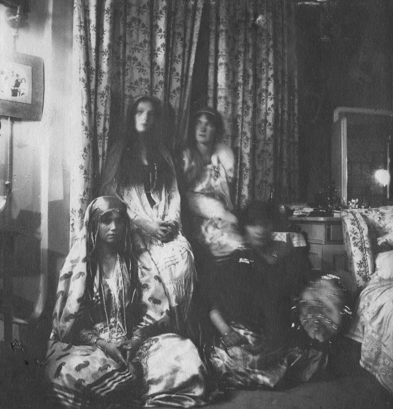 Four young women in fancy dress sprawled across a bedroom floor and furniture