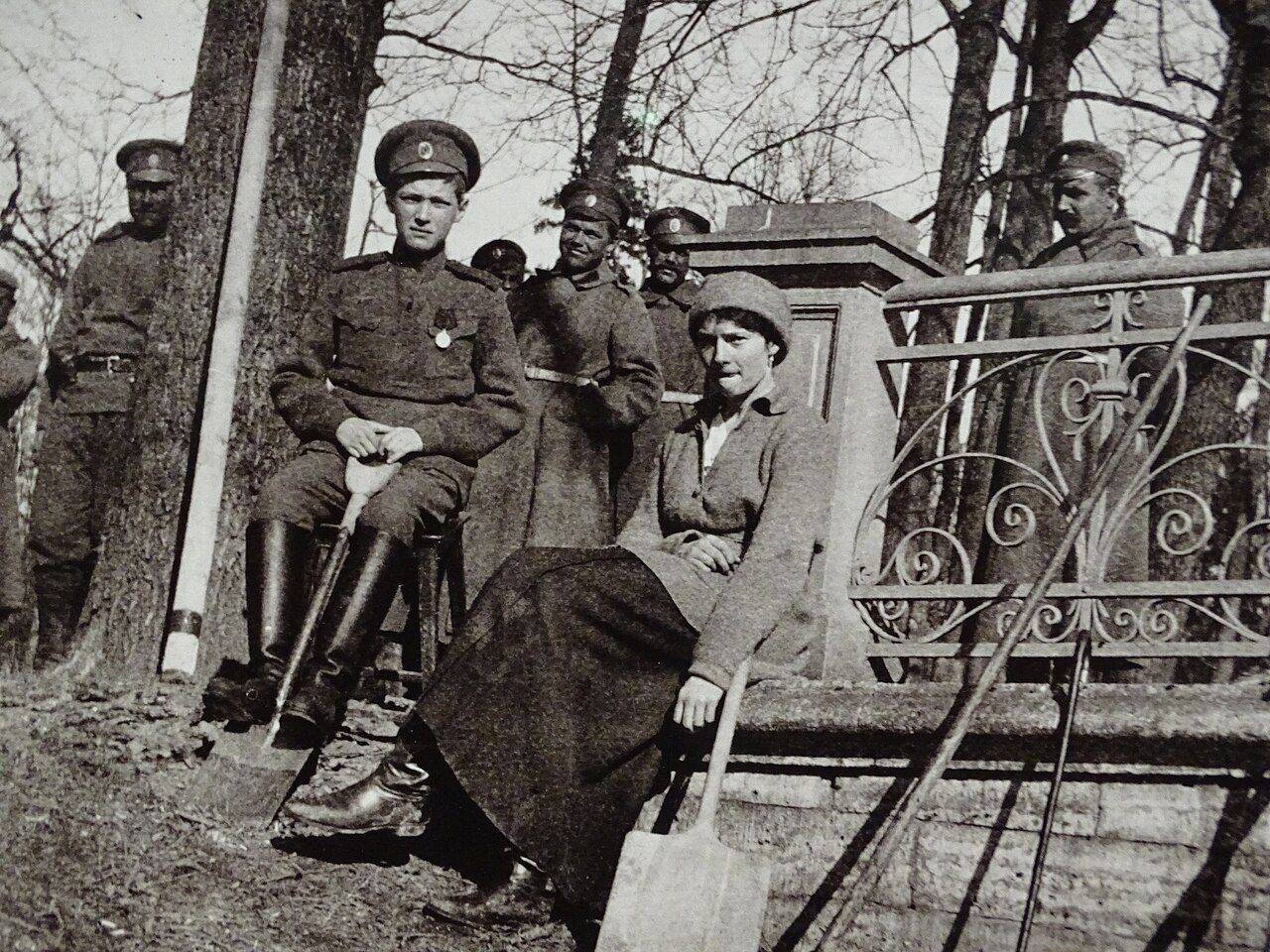 Soldiers standing about while figures work at the ground in a park