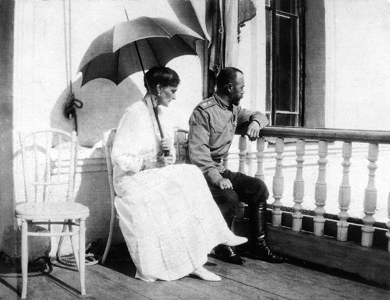 A man and a woman with a parasol sitting together on a balustrade