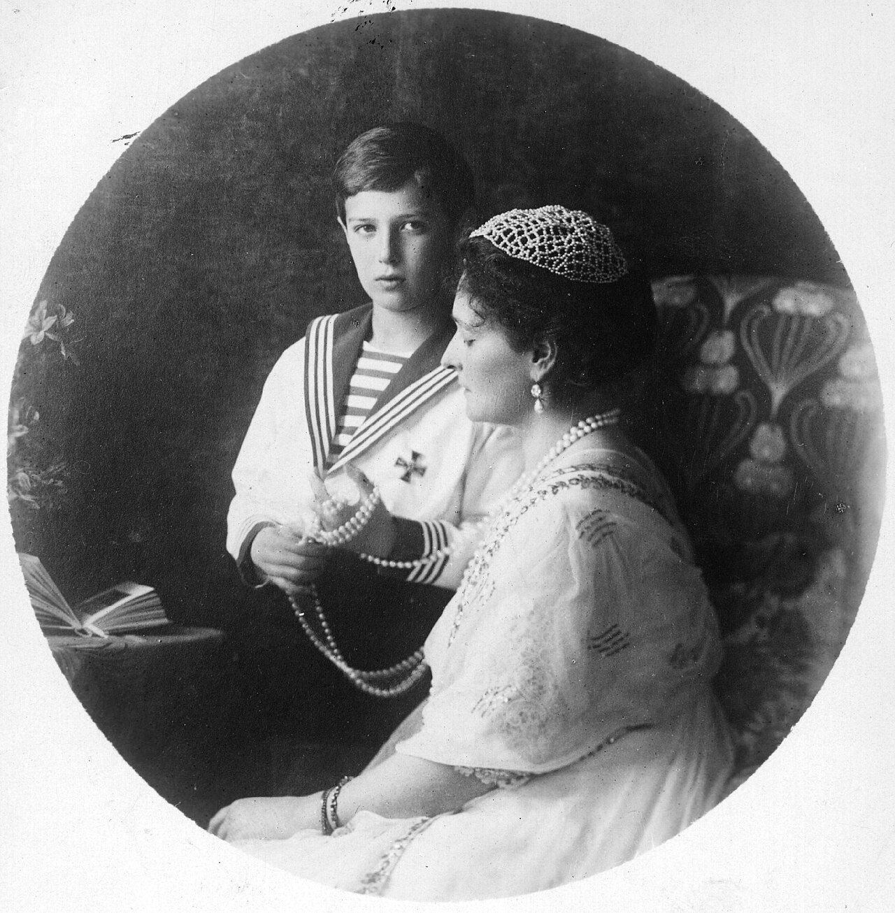 Oval portrait of a woman holding a small child who is playing with her pearls