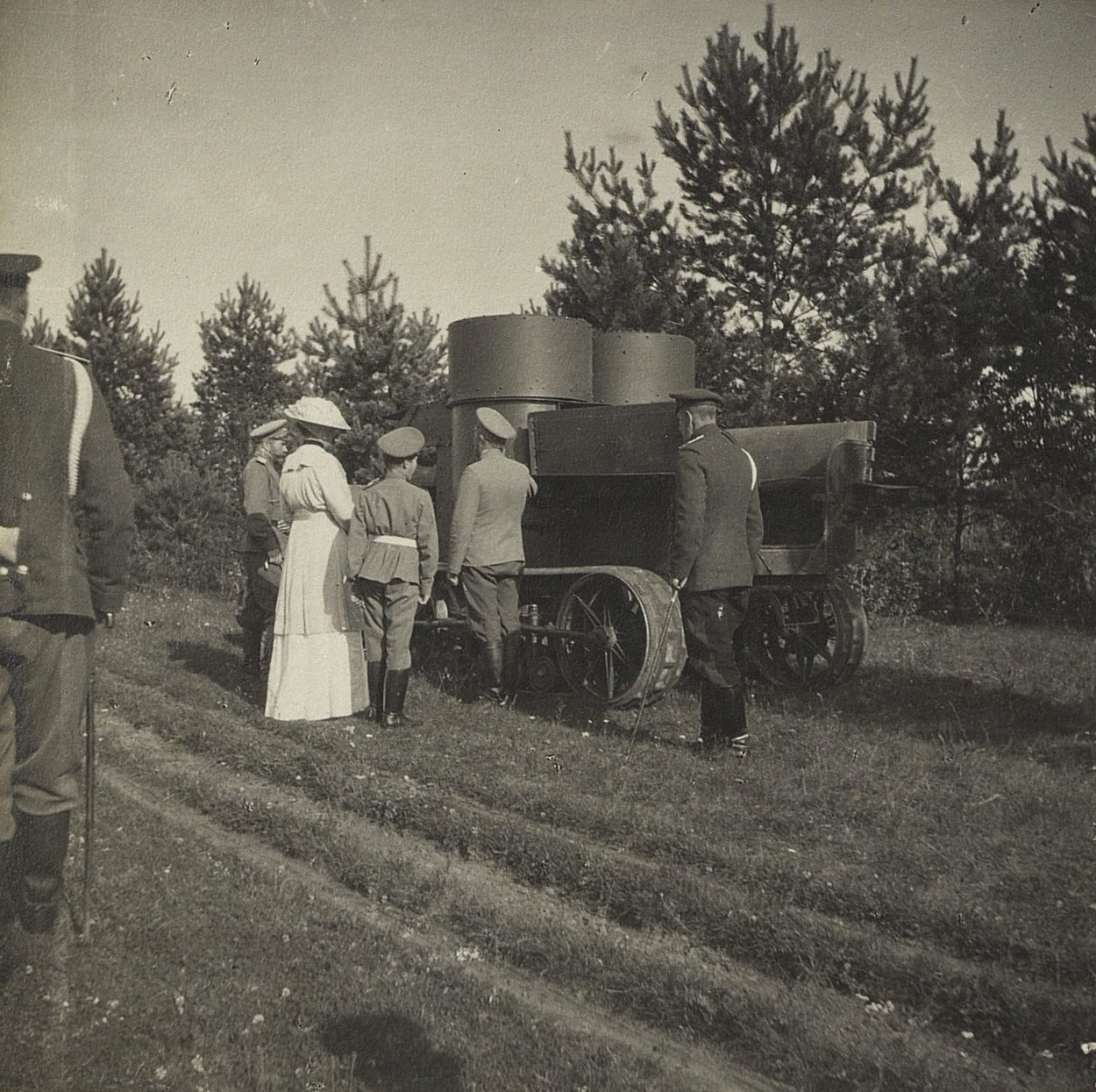 Figures in light summer clothes standing beside a tracked armoured car in a field