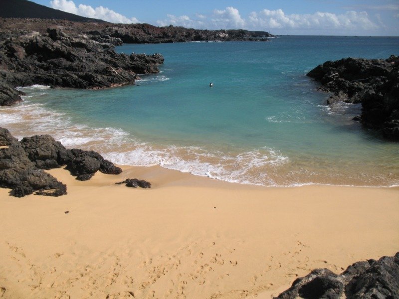 A small sandy beach enclosed by black lava rock at Comfortless Cove, Ascension Island, with turquoise water