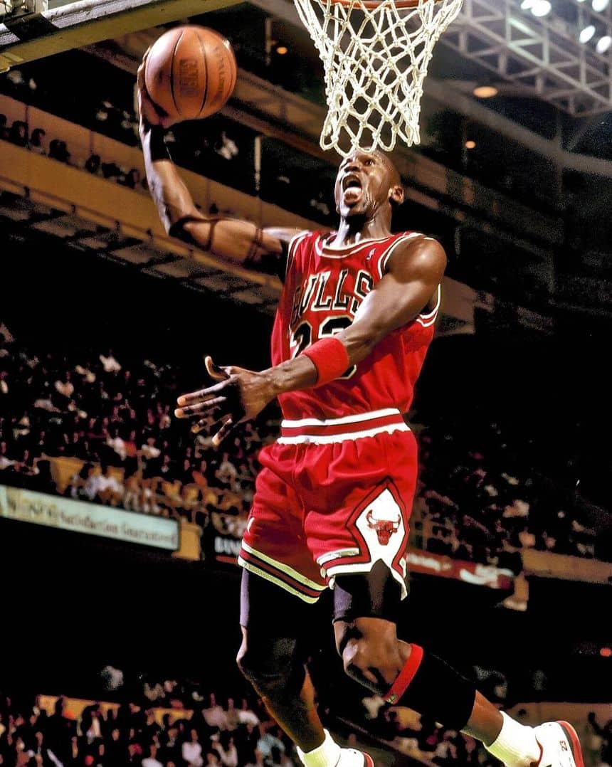 Michael Jordan in a red Chicago Bulls uniform rising toward the rim with the ball cocked behind his head