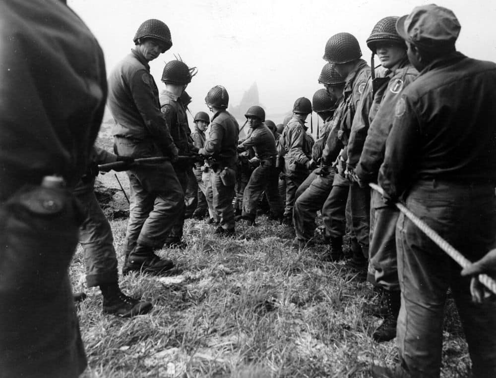 A long line of helmeted American and Canadian soldiers hauling on a rope in thick fog on a grassy slope above Lily Beach, Kiska