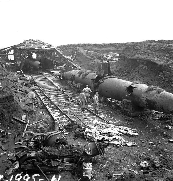 Soldiers standing on a marine railway beside two abandoned Japanese submarines and a wrecked shed on Kiska Island