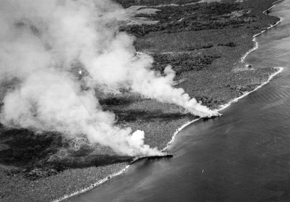 Two beached Japanese transport ships burning on a shoreline