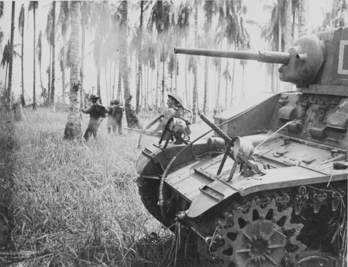 Australian infantrymen advancing beside a light tank through coastal scrub