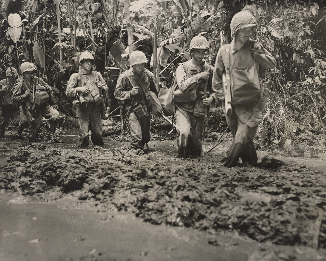 Marines picking their way along a deep muddy jungle track in single file