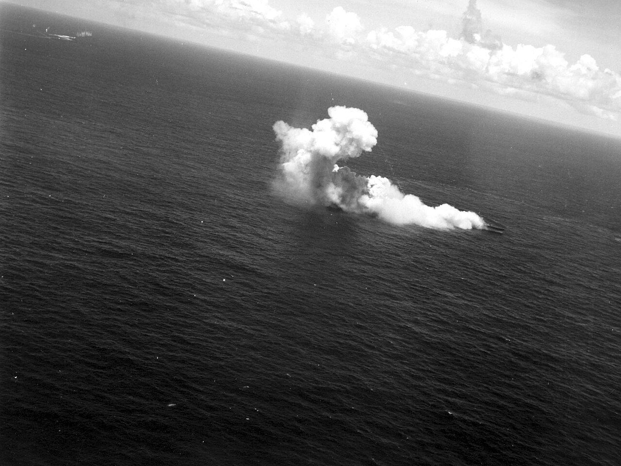 A Japanese light cruiser burning and listing, seen from an attacking aircraft