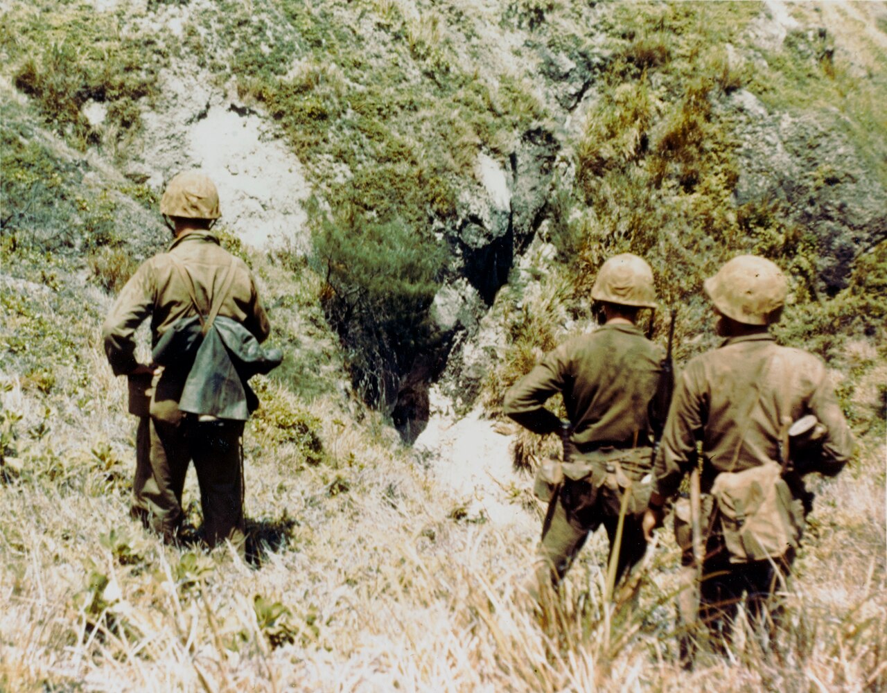 Marines moving across broken limestone and coral ground carrying rifles