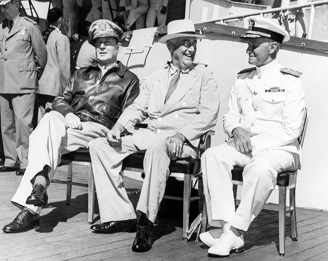 Four senior American leaders seated and standing around a wall map aboard a warship