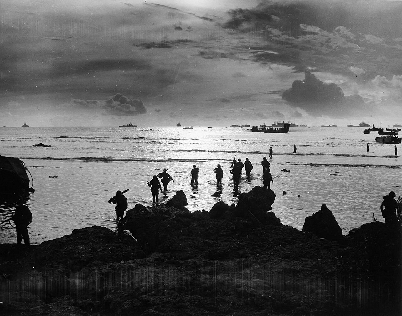 Troops wading through shallow surf toward a beach from landing craft