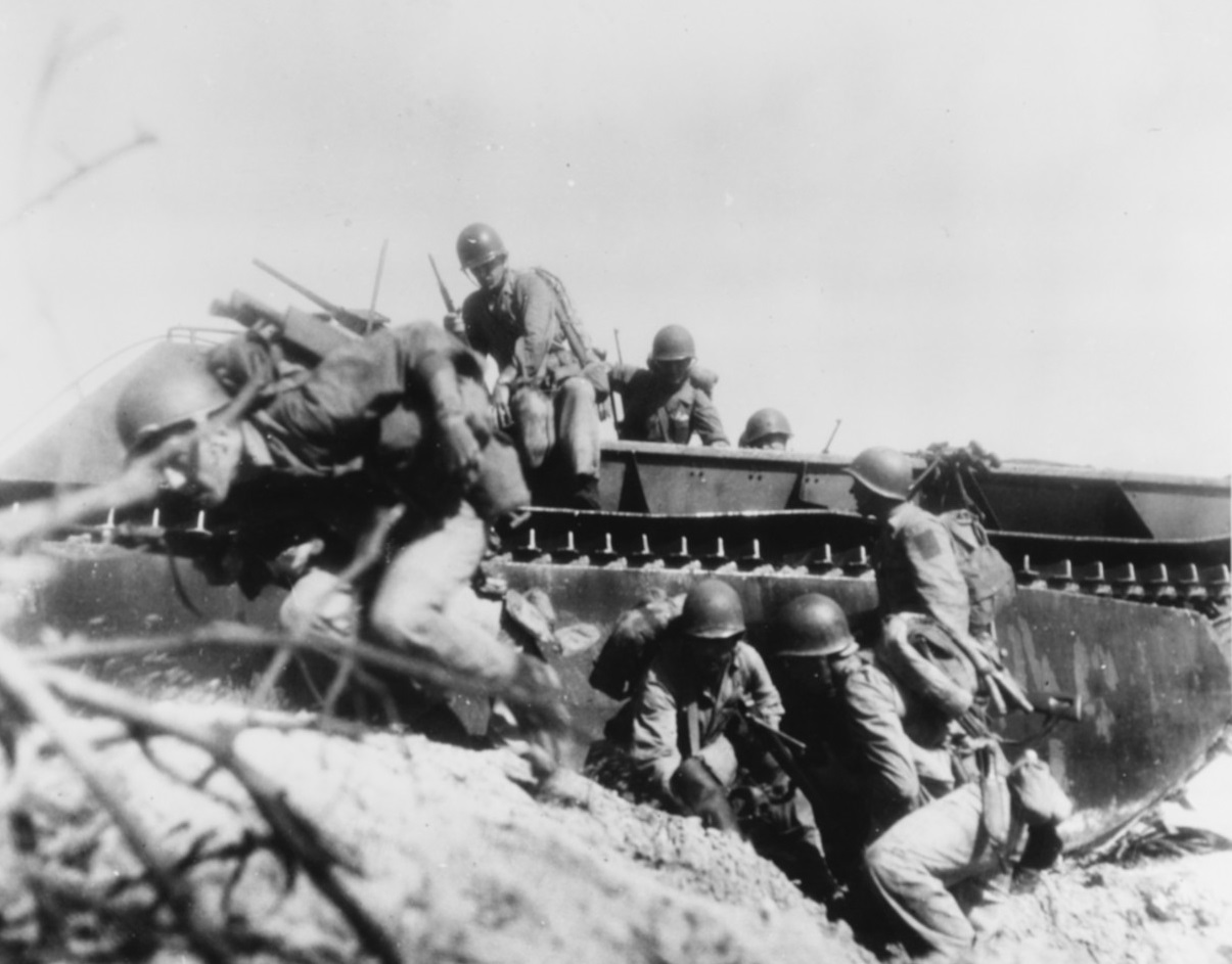 Marines dismounting from an amphibious tractor and taking cover on a beach