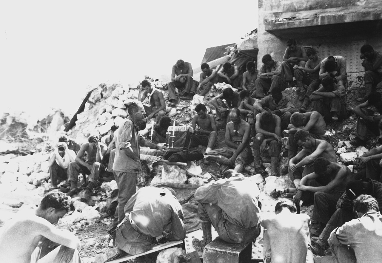 A chaplain holding an open-air service for troops seated on the ground