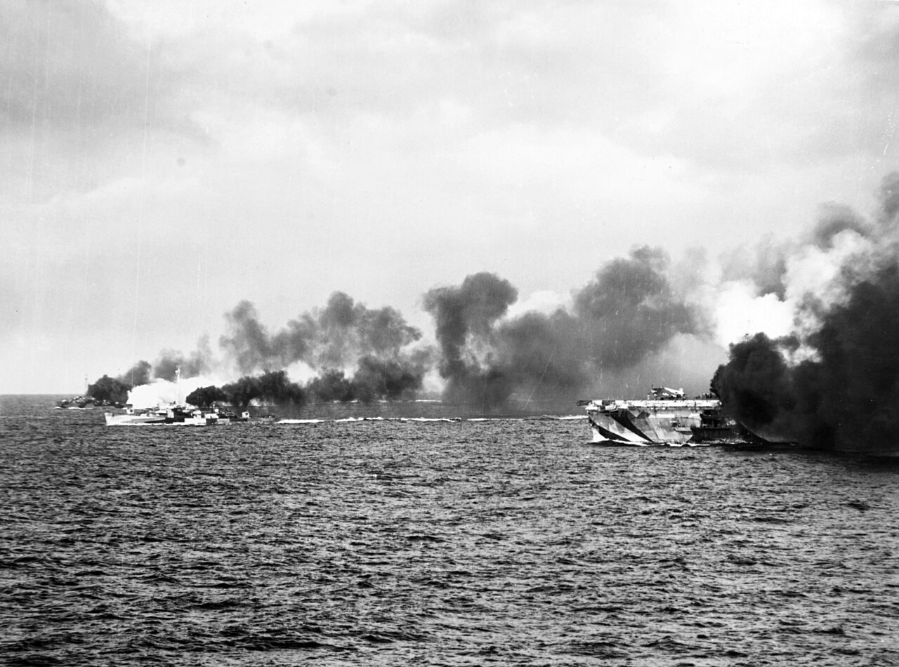 An escort carrier and destroyers laying a smoke screen at sea
