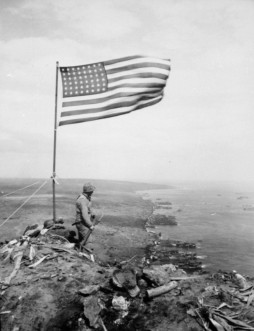 An American flag flying from a pole on the bare crest of a volcanic peak