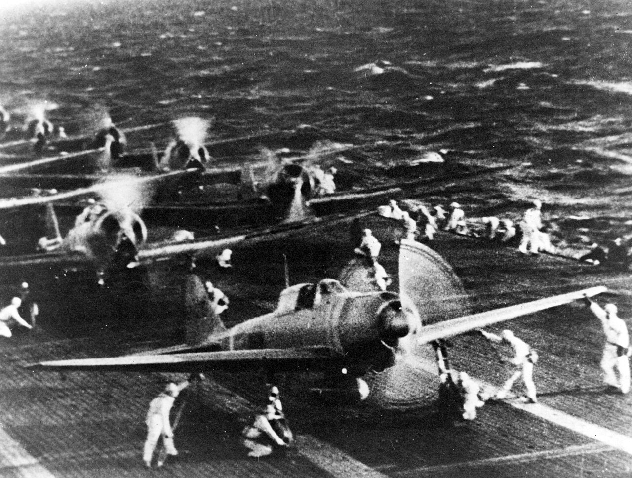 Japanese naval aircraft with engines running on a carrier flight deck, crewmen waving them off