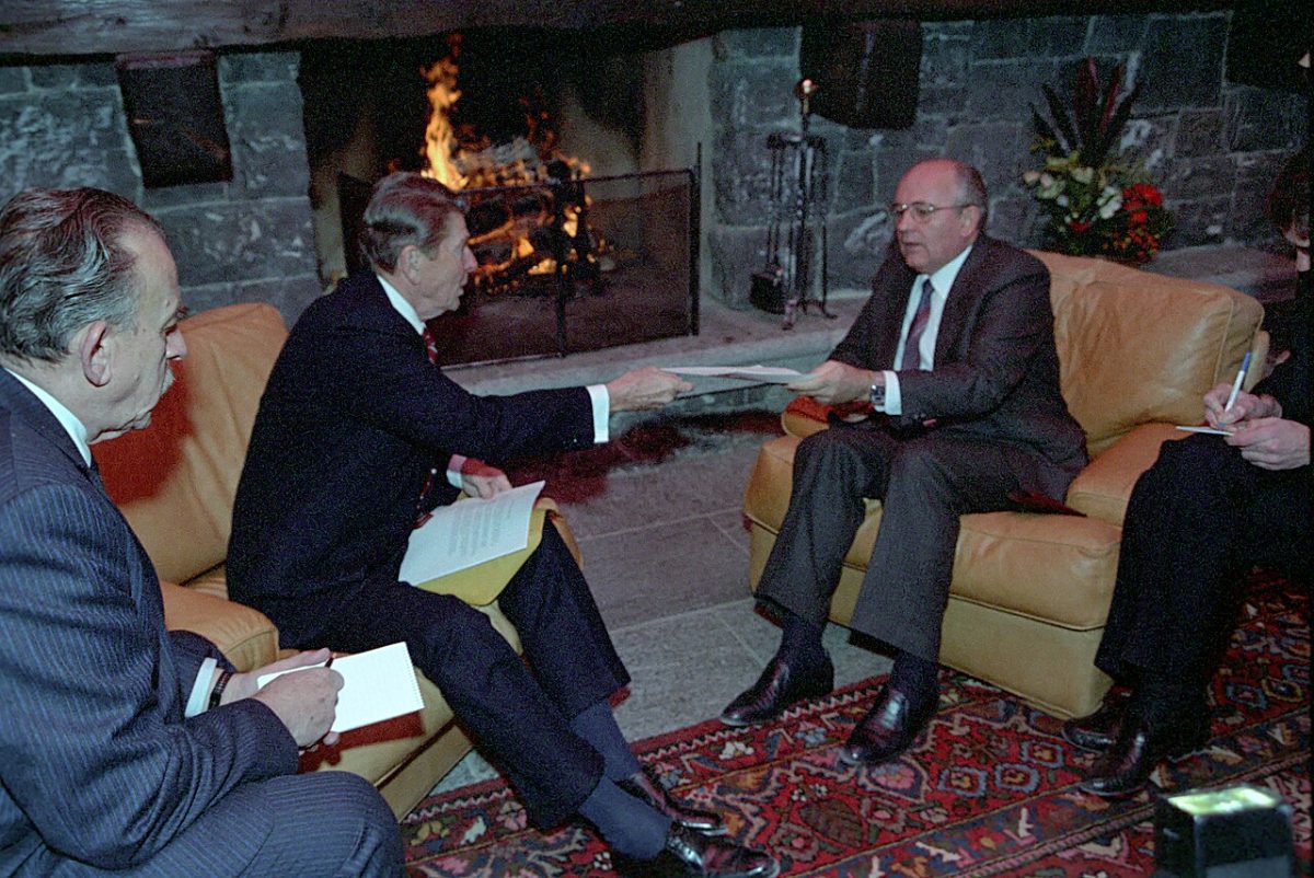 Reagan and Gorbachev seated in armchairs in front of a stone fireplace at the Fleur d'Eau pool house in 1985, each with an interpreter taking notes