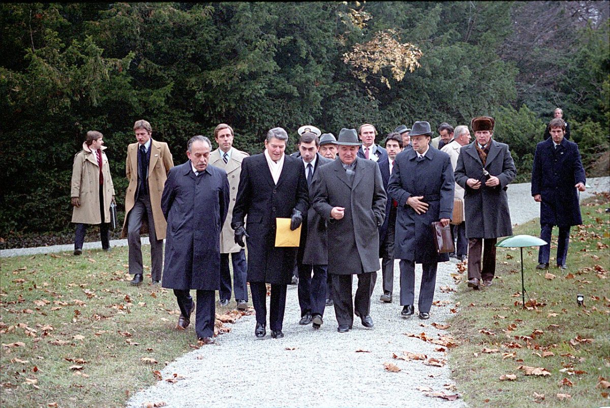 Reagan and Gorbachev walking side by side down a gravel path through autumn leaves at Fleur d'Eau, followed by aides, interpreters and security