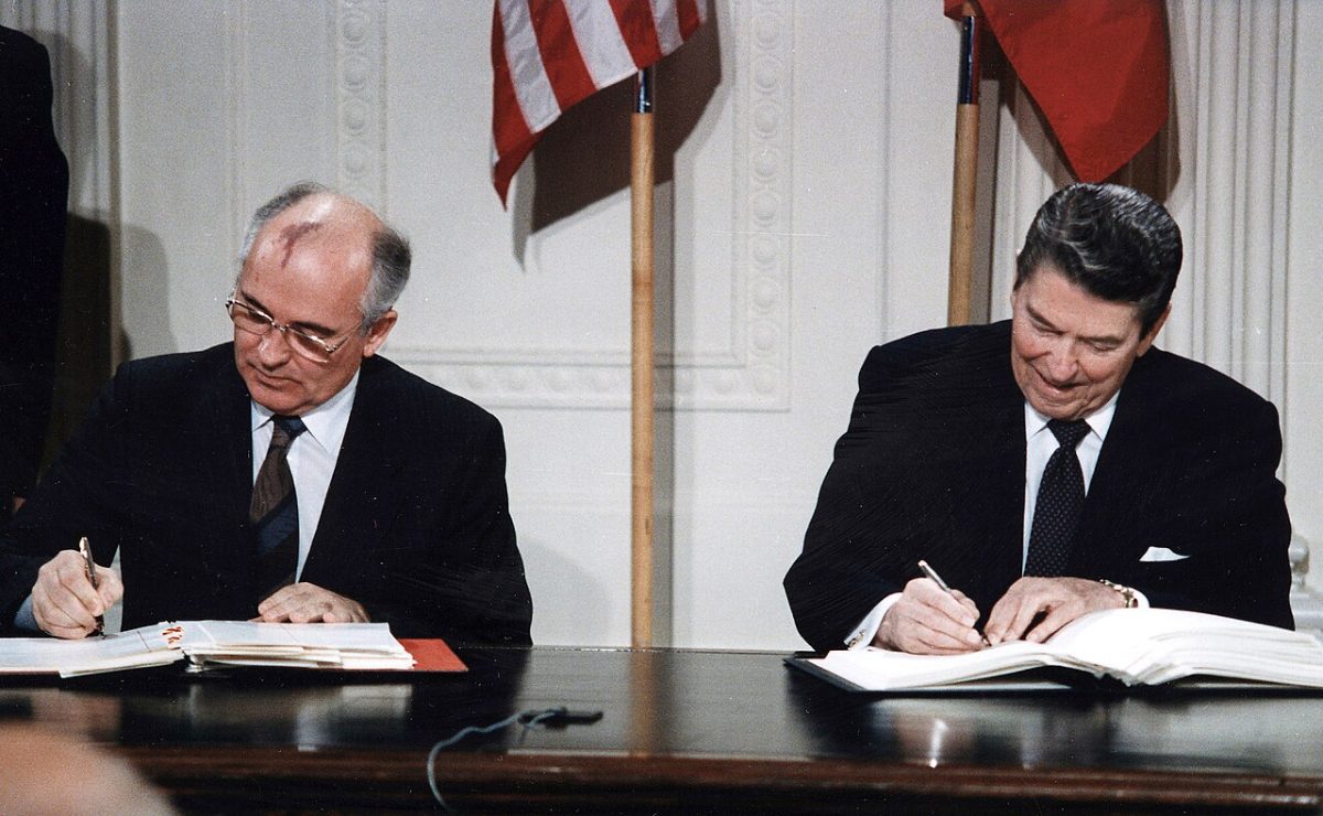 Gorbachev and Reagan seated side by side signing the INF Treaty in the East Room of the White House in December 1987, flags behind them