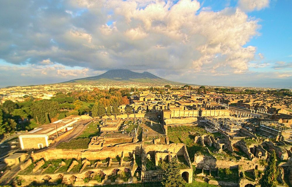 Aerial view of the excavated ruins of Pompeii at golden hour with Mount Vesuvius rising behind the city