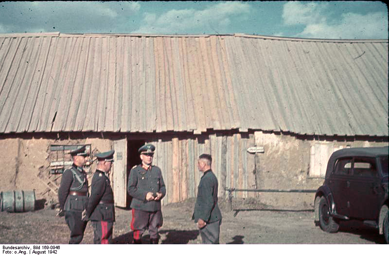 German officers standing in conversation beside a building and a staff car