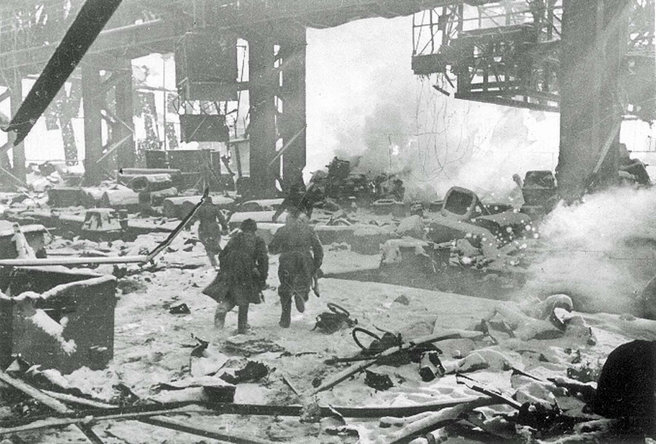 Soldiers moving through a vast factory workshop strewn with wreckage and smoke