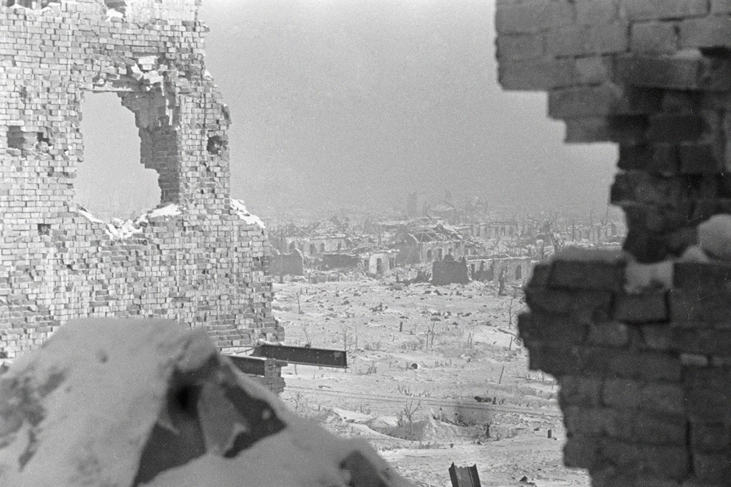 A snow-covered city of ruins seen through a shell hole in a brick wall