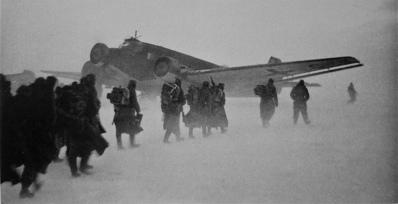 German soldiers trudging through snow beside a three-engined transport aircraft