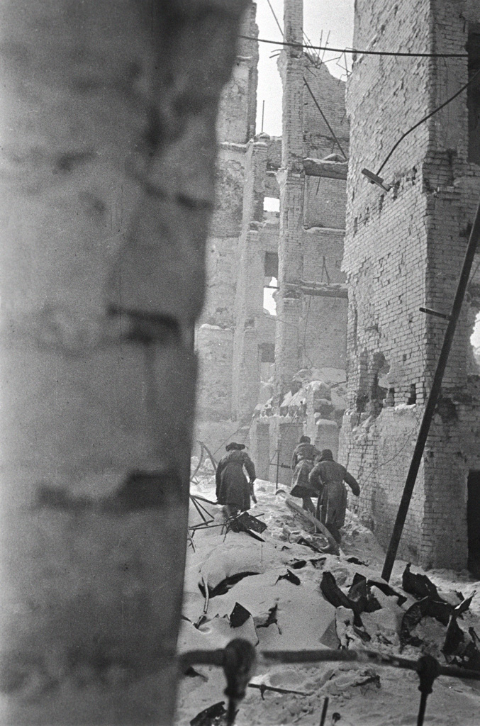 Soldiers picking their way down a snow-covered alley between gutted brick buildings