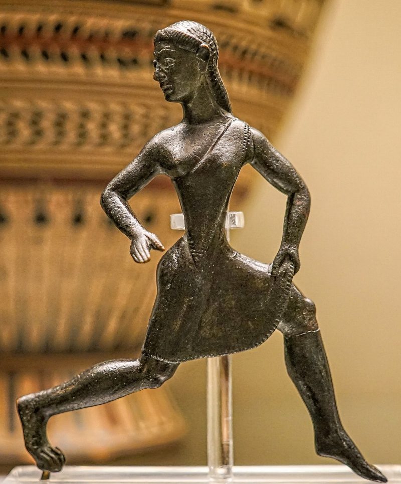 A small archaic Greek bronze of a girl running in a short tunic, arms bent, one leg extended behind her