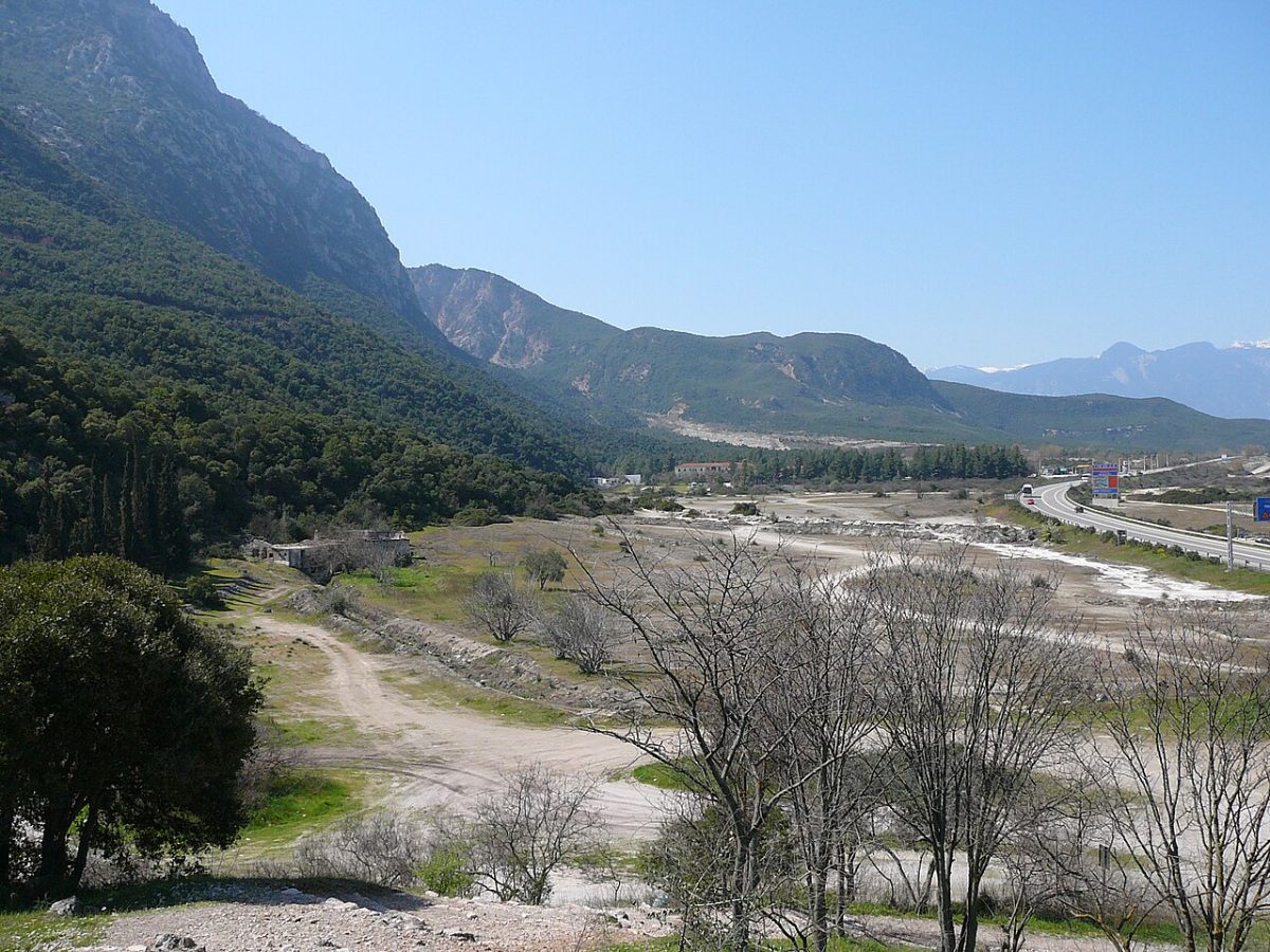 The plain at Thermopylae today, a wide flat expanse of pale ground between a steep wooded mountain and a modern motorway